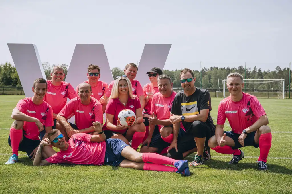 Mieszana drużyna piłkarska pozuje do zdjęcia grupowego po zakończonym meczu, prezentując sportową integrację uczestników.