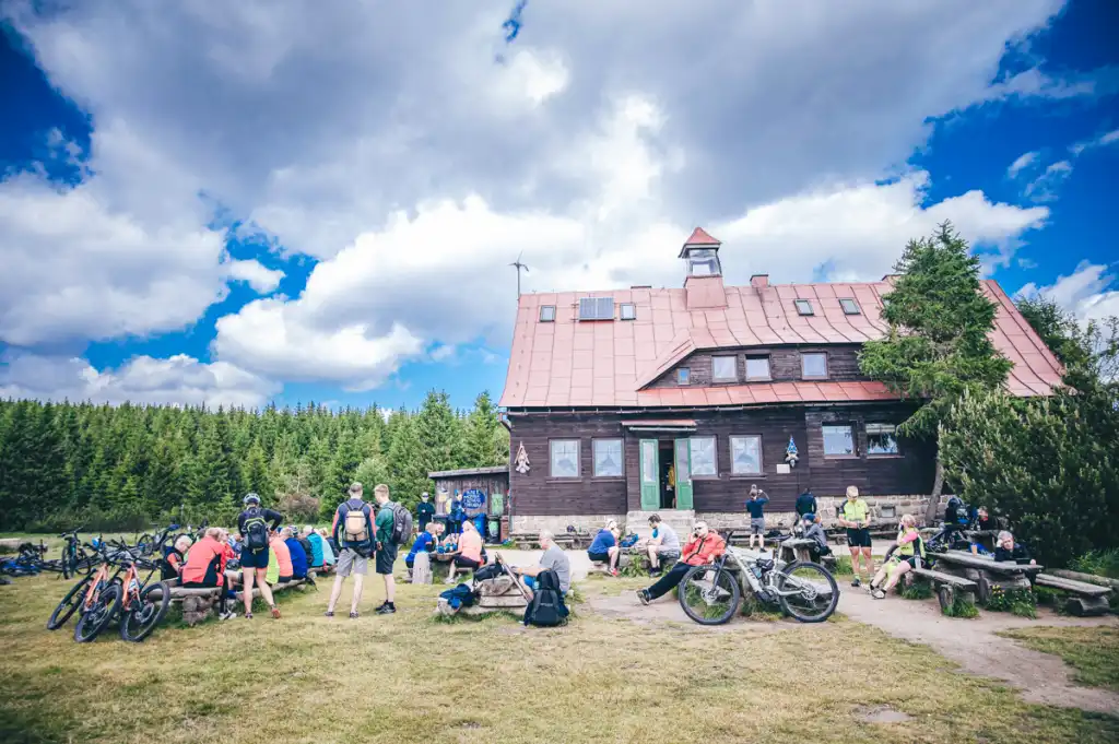 Grupa rowerzystów odpoczywa przy górskim schronisku, zatrzymując się na przerwę podczas eventu terenowego.