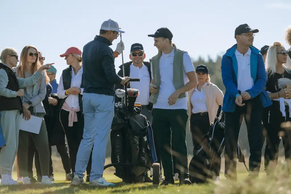 Event z serii Piąty Żywioł Ziemia z Jerzym Dudkiem odkładającym kij do wózka, podczas gdy uczestnicy stoją na polu golfowym.