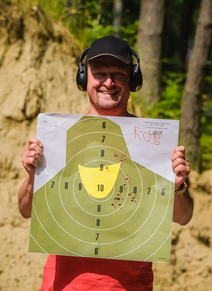 Uśmiechnięty uczestnik prezentuje swoją tarczę strzelecką.