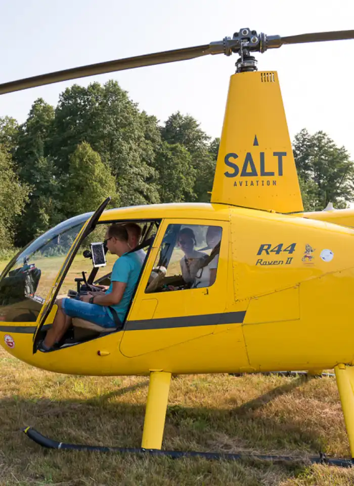 Uczestnik wsiada do śmigłowca podczas części praktycznej wydarzenia lotniczego, ujęcie wykonane z bliska przy kabinie.
