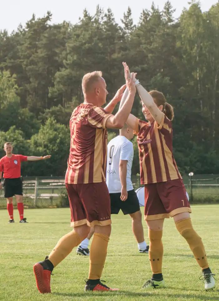 Zawodnik i zawodniczka przybijają sobie piątkę na boisku, celebrując udaną akcję i dobrą współpracę w trakcie turnieju.