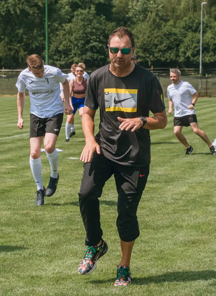 Jerzy Dudek prowadzi dynamiczną rozgrzewkę uczestników turnieju, przygotowując drużyny do sportowej rywalizacji na boisku.