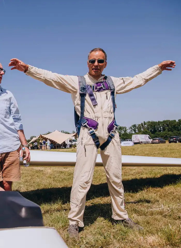 Sebastian Kawa pozuje w kombinezonie lotniczym, rozkładając ręce niczym skrzydła szybowca podczas spotkania z uczestnikami.