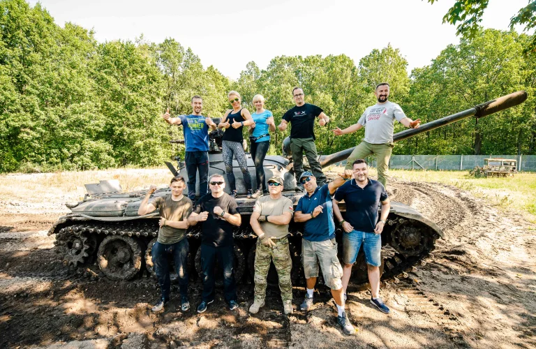 Grupa uczestników na evencie motywacyjnym Piątego Żywiołu pozuje do zdjęcia na tle czołgu, w środku Krzysztof Przepiórka.