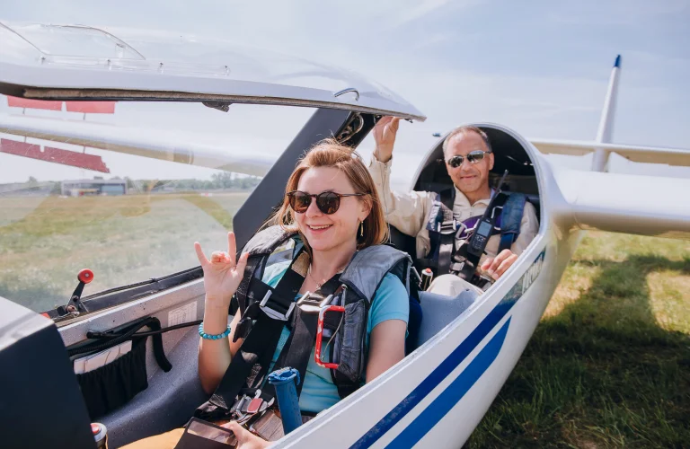 Sebastian Kawa siedzi w kabinie szybowca z uśmiechniętym uczestnikiem, przygotowując się do lotu. 15.