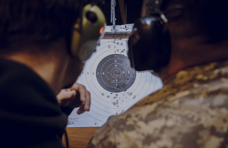 Uczestnik i instruktor omawiają wyniki strzelania, trzymając tarczę strzelecką.