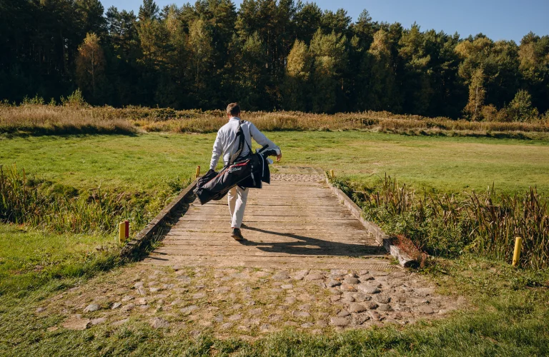 Event z serii Piąty Żywioł Ziemia, gdzie uczestnik przechodzi mostek na polu golfowym z torbą pełną kijów.