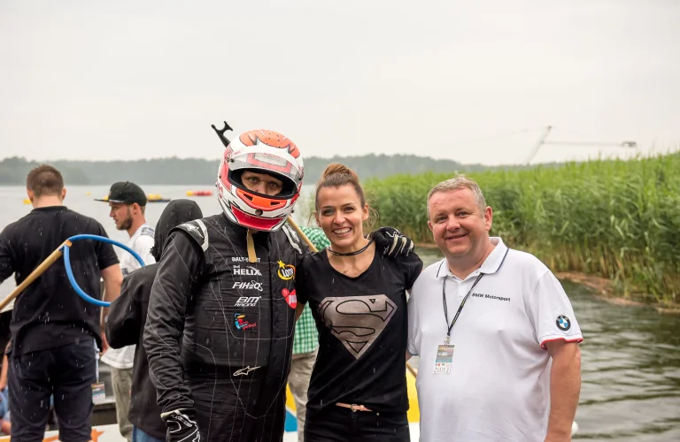 Grupa uczestników pozuje do wspólnego zdjęcia z Bartkiem Marszałkiem na tle jeziora po zakończonym przejeździe.