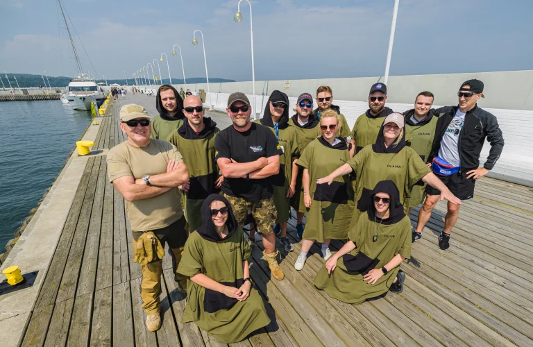 Grupa uczestników w wojskowych ręcznikach pozuje do zdjęcia na molo.