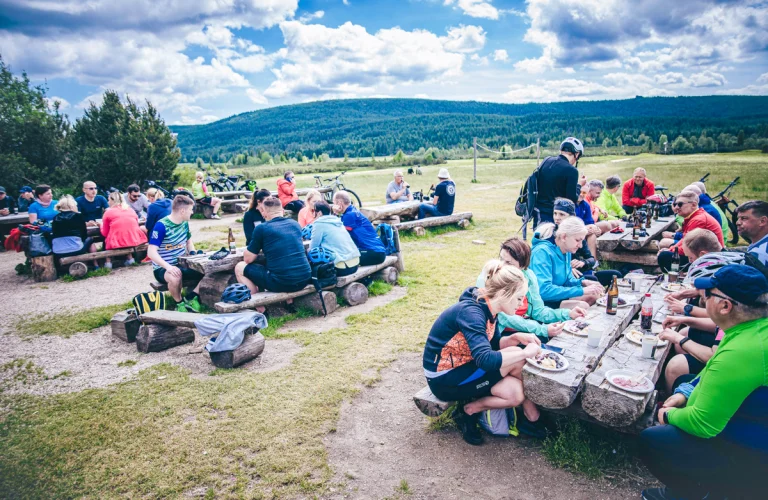 Uczestnicy robią przerwę na posiłek, siedząc na polanie podczas części regeneracyjnej eventu rowerowego.