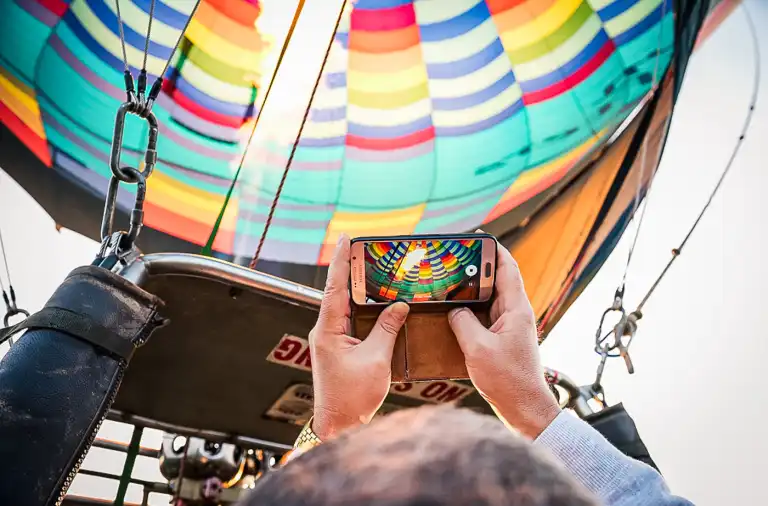 Balon na gorące powietrze wznosi się nad ziemię, a uczestnicy stoją w koszu podczas startu eventowego.