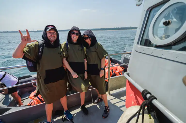 Troje uczestników pozujących na okręcie na tle morza.