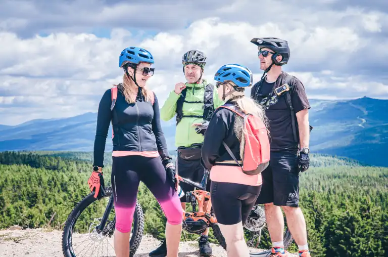 Uczestnicy stoją z rowerami na punkcie widokowym, podziwiając górską panoramę po zakończeniu odcinka trasy.