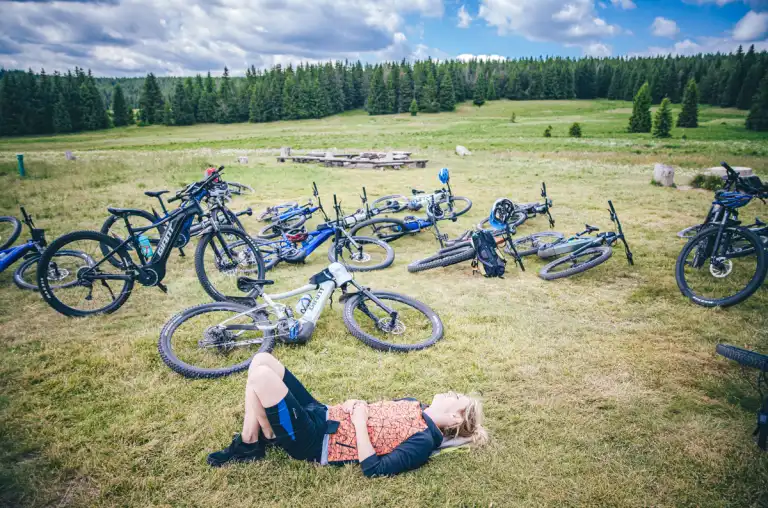 Uczestnik odpoczywa na polanie na tle zaparkowanych rowerów, robiąc przerwę po intensywnym odcinku trasy.