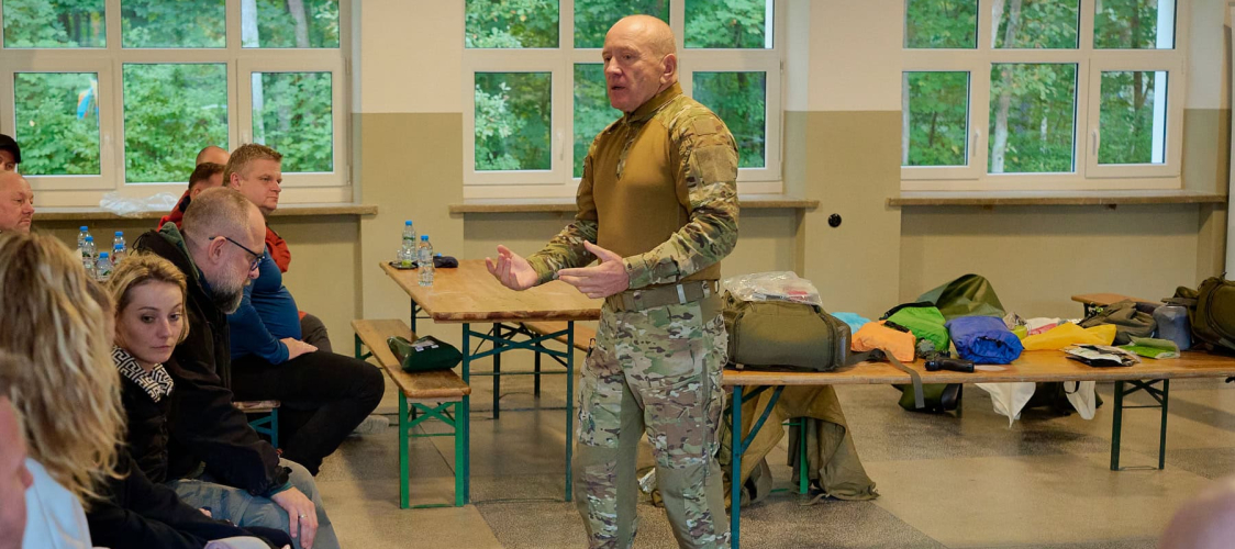 Instruktor omawia z uczestnikami przygotowanie kryzysowe podczas szkolenia z plecaka ewakuacyjnego, na stołach plecaki