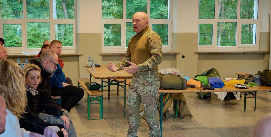 Instruktor omawia z uczestnikami przygotowanie kryzysowe podczas szkolenia z plecaka ewakuacyjnego, na stołach plecaki