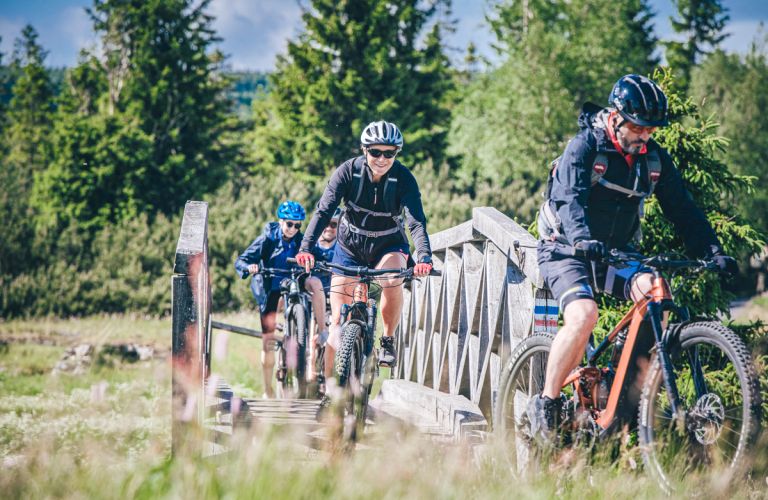 Rowerzyści podążają przez polanę otoczoną lasem, pokonując kolejny fragment górskiej trasy.